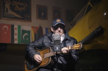 man and guitar in front of Harvard airplane