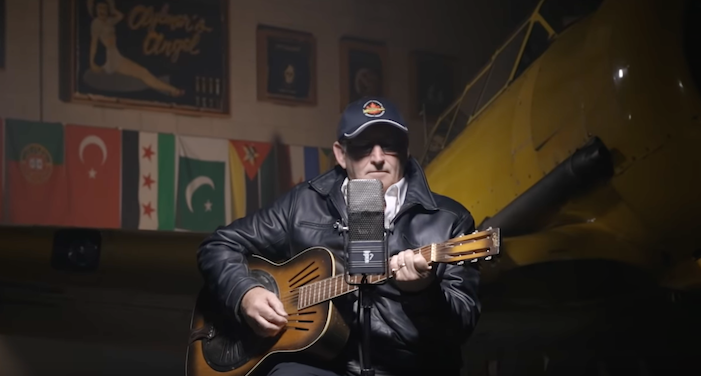man and guitar in front of Harvard airplane